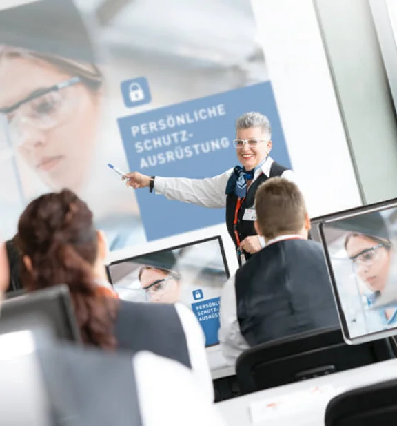 lächelde Frau die auf eine Schulung "Persönliche Schutzausrüstung" zeigt wird aufmerksam von einigen Menschen angehört die an der Schulung teilnehmen