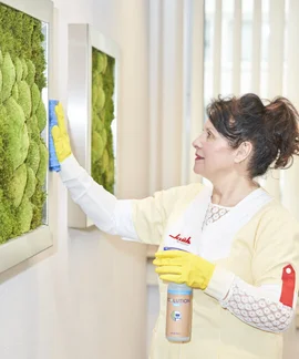 Klüh Cleaning Reinigungskraft in Arbeitskleidung mit gelben Gummihandschuhen wischt mit einem Tuch 