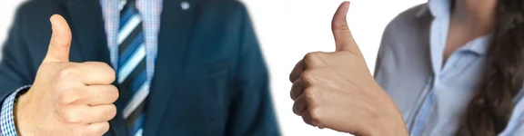 Ein Mann im Anzug und eine Frau im Hemd stehen nebeneinander und zeigen ihren Daum hoch